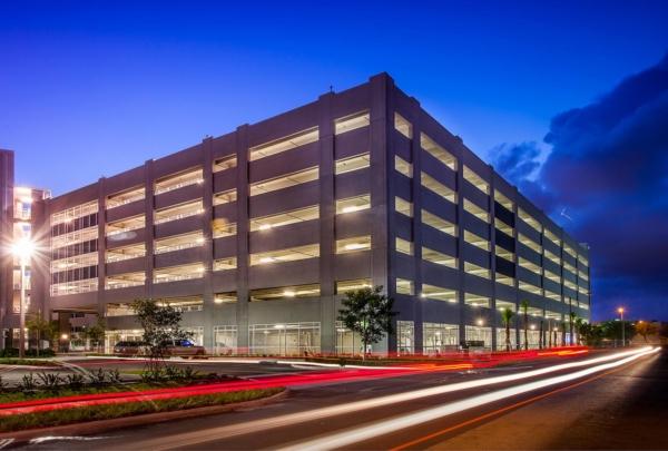 迈阿密戴德学院海厄利亚校区停车场的外部照片. Evening photo with bright blue skies. Garage lights on. Vehicle lights create streaks on the adjacent street.